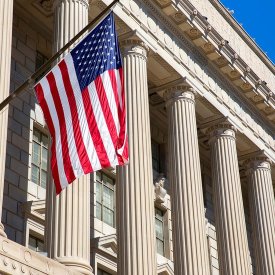 A closeup of a government building with pillars visible and the America flag hanging from a pillar