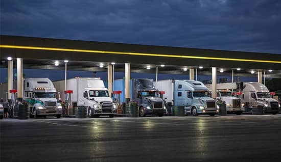 A row of semi trucks at the fuel station at night