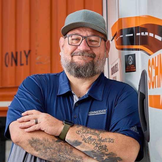 Schneider driver leaned against door of semi-truck tractor with orange container in the background