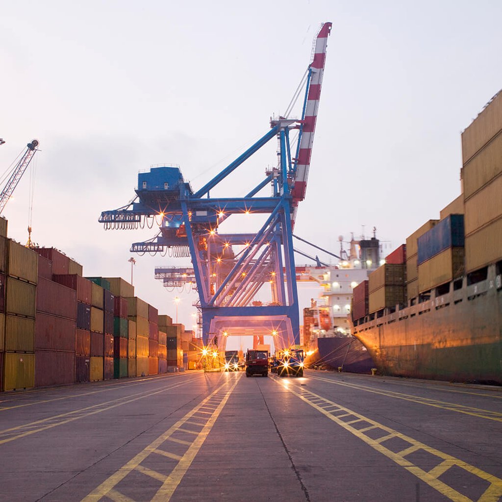 Vehicles driving through port drayage dock with cargo containers stacked on both sides