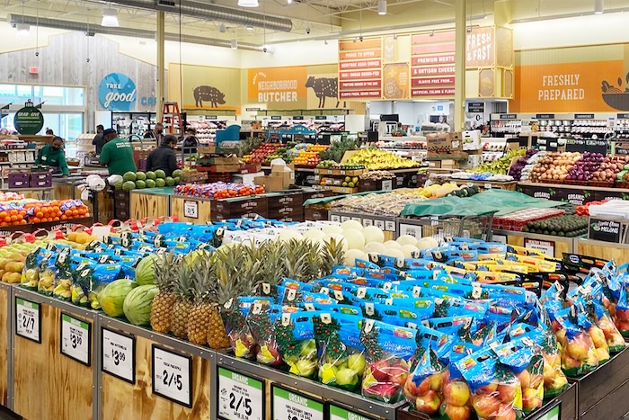 Grocery store interior looking across isles of fresh produce, including red and green apples, pineapples, watermelons, and more.
