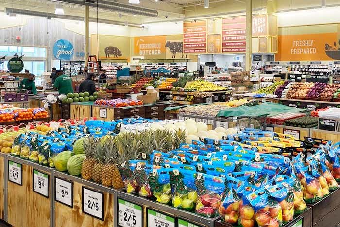 Grocery store interior looking across isles of fresh produce, including red and green apples, pineapples, watermelons, and more.