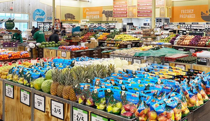 Grocery store interior looking across isles of fresh produce, including red and green apples, pineapples, watermelons, and more.