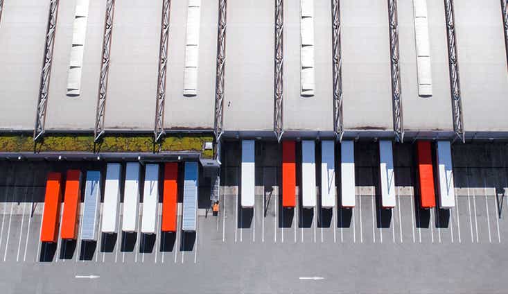 An aerial view of a large warehouse with multiple white and orange trailers sitting at docks