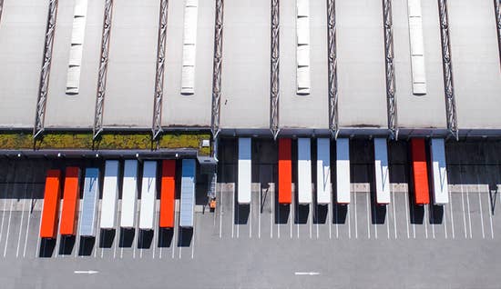 An aerial view of a large warehouse with multiple white and orange trailers sitting at docks
