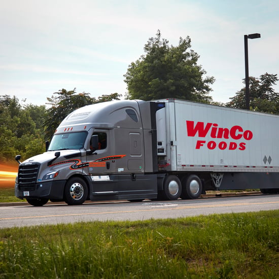 A large semi-truck on the road, with trees lining the highway under a clear sky