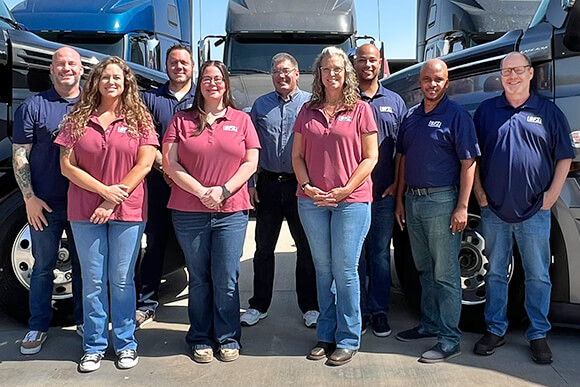 A group of people standing in front of a row of semi trucks