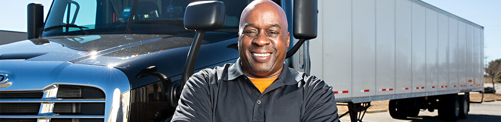 An owner-operator smiles with arms crossed confidently as he poses in front of his truck