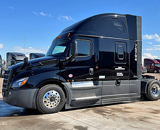 A sleek, black semi-truck is parked outdoors, showcasing its modern design and clean appearance under a clear sky. The truck has a streamlined shape with aerodynamic features, and the number “7594” is visible on its side. 