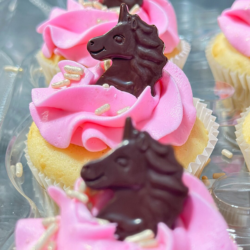 A row of pink icing cupcakes with chocolate unicorns on top. 
