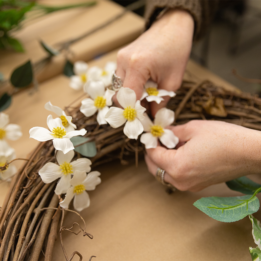 hands adding white flowers to grapevine wreath