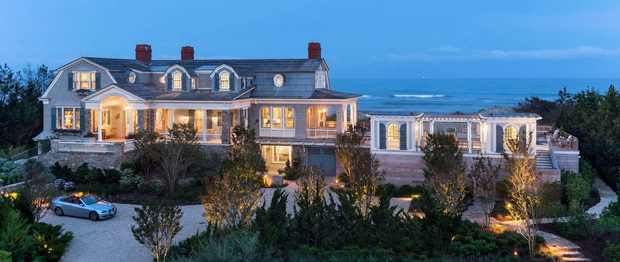 a luxury hamptons home at dusk with the ocean view behind