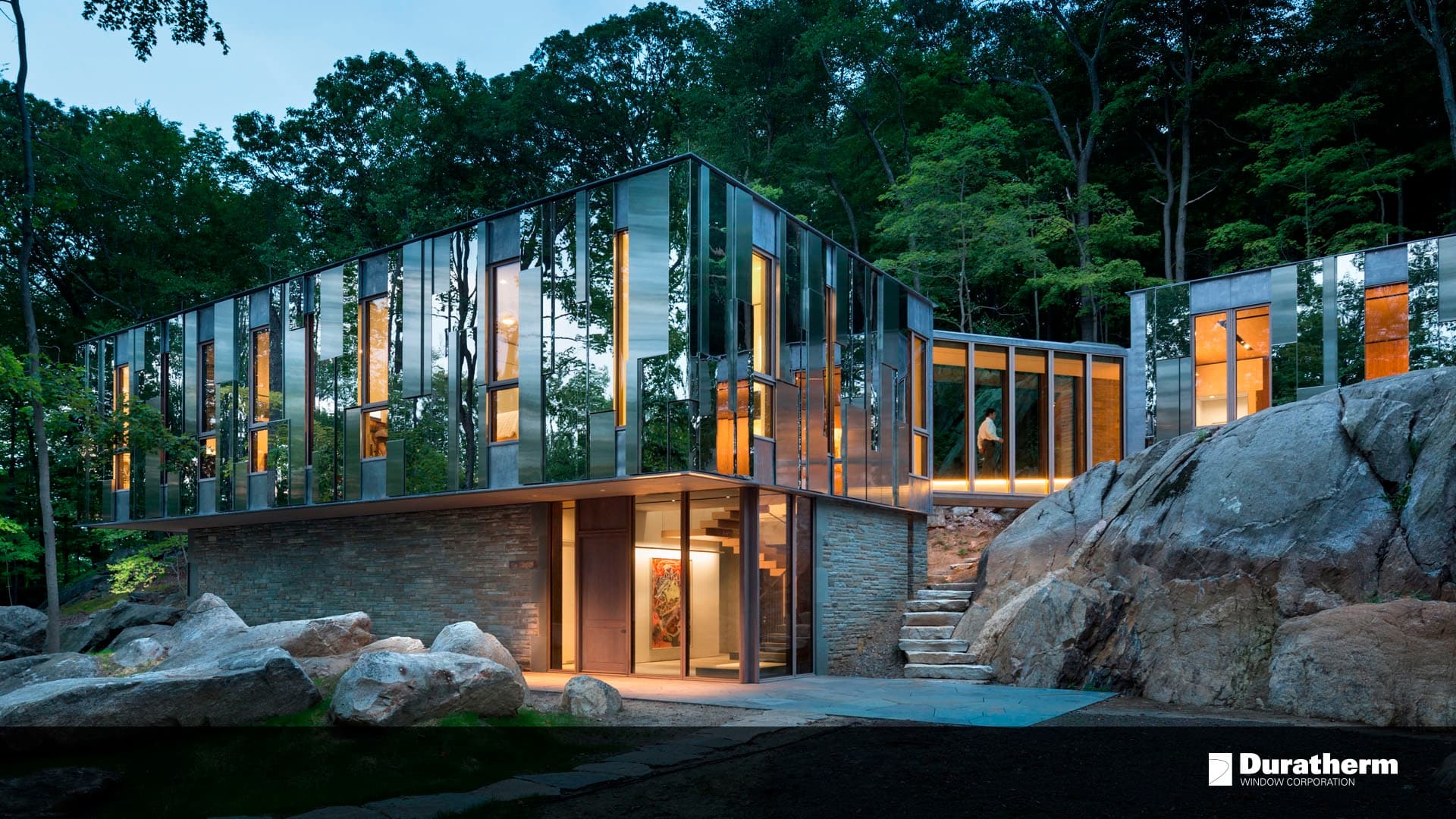 home in the middle of a forest with clear and reflecting glass as the walls