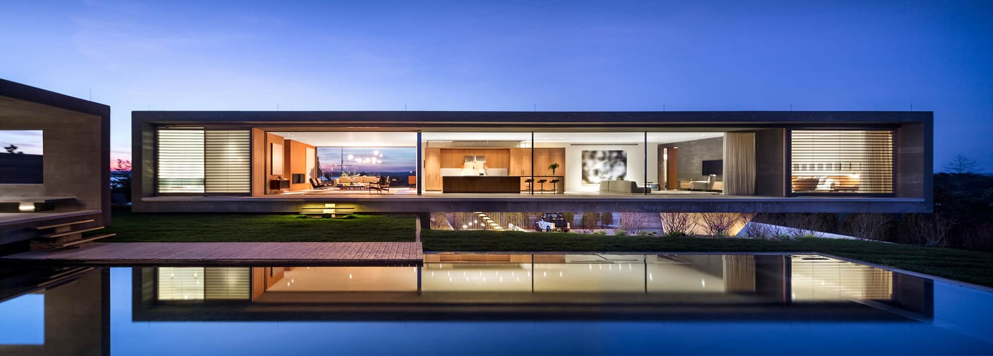 the light from inside a contemporary home reflects off the infinity pool outside