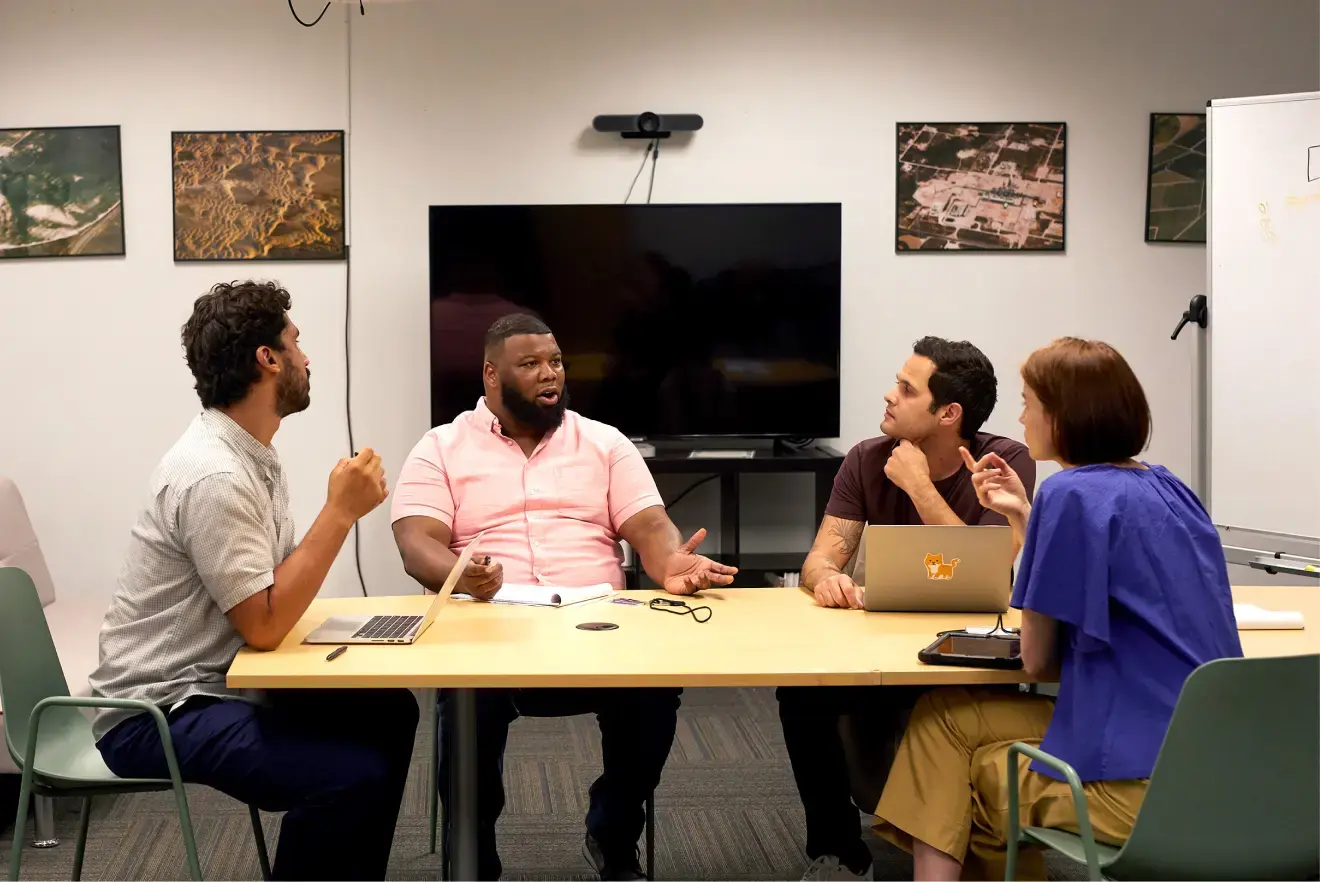 the man sits at a conference table with three of his colleagues as they discuss Indeed’s products for hiring the warehouse workers they need