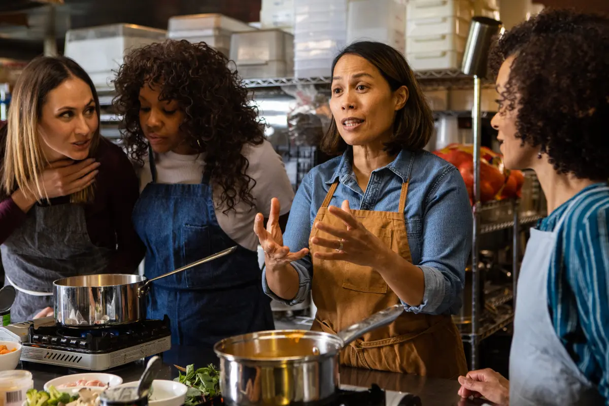 The owner teaches three of her employees how to make a recipe as they stand in the restaurant’s kitchen