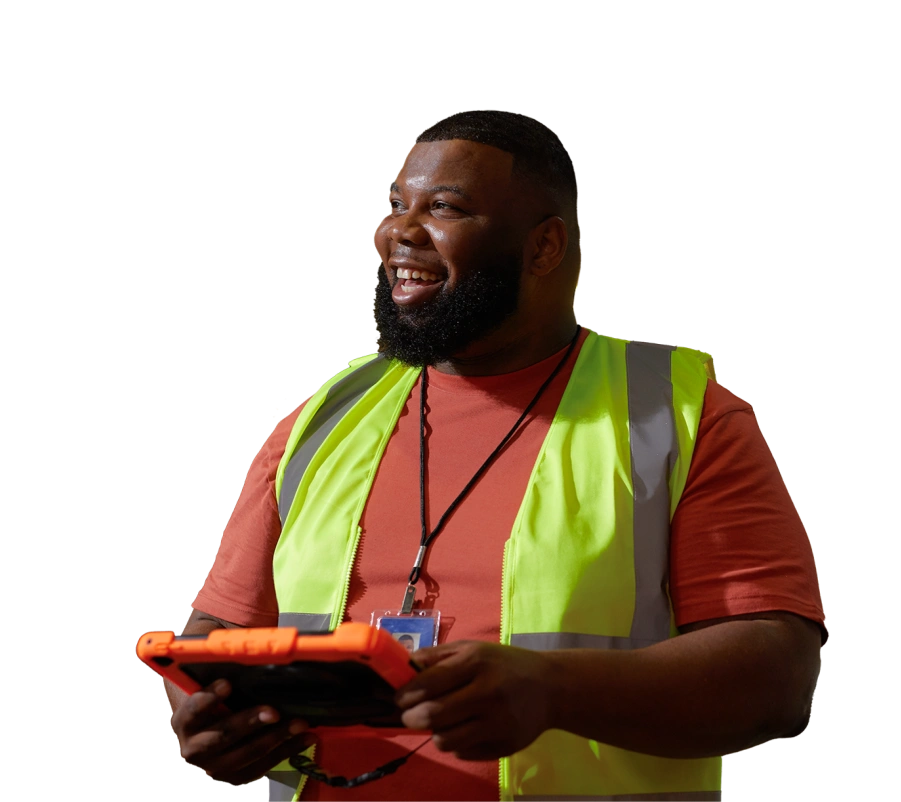 a smiling man with dark hair and beard wears a reflective vest and holds an orange tablet in a warehouse