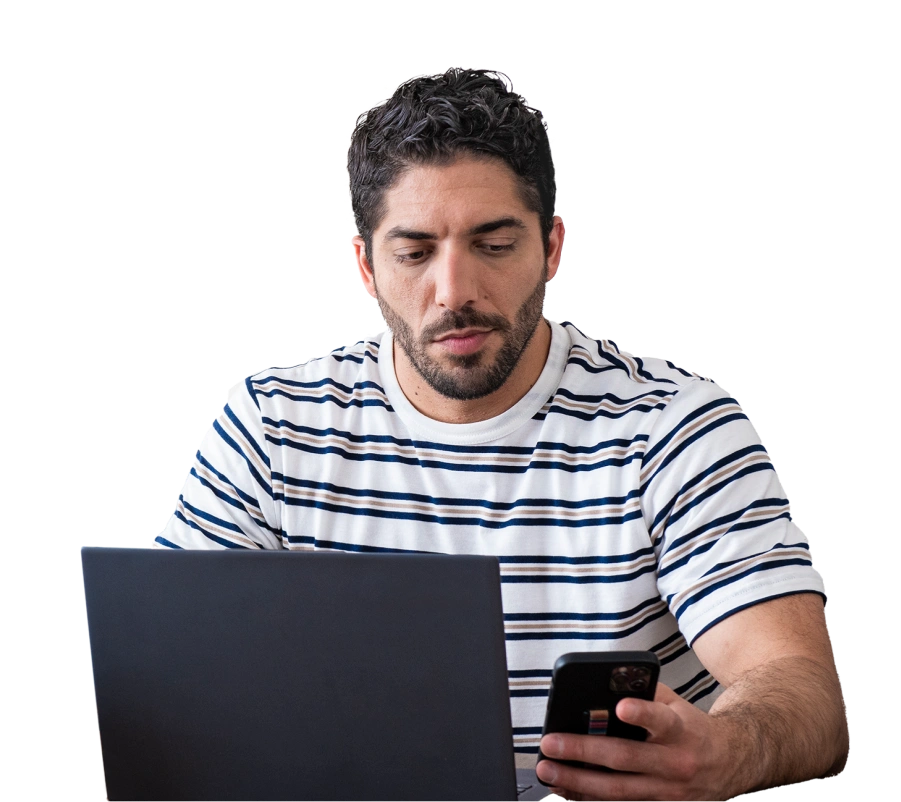 a man in a striped shirt on his phone and computer preparing to interview with an employer on Indeed
