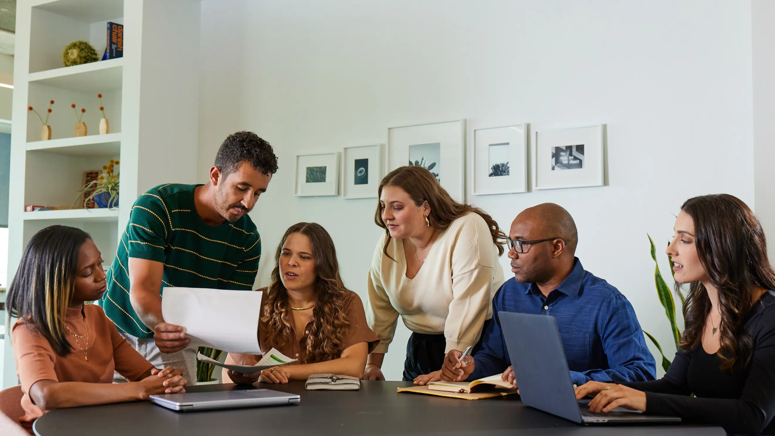 A group of coworkers at a small business sits around a circular table and look at work one of them has brought for discussion
