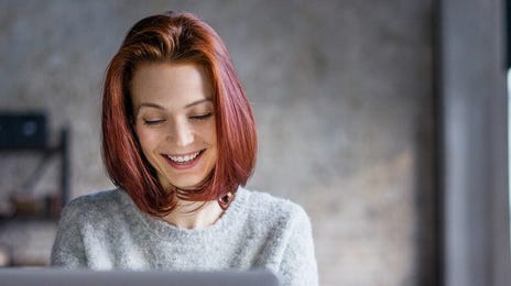 Girl in her room sitting in front of a laptop and smiling during an online English lesson with Berlitz Lyon