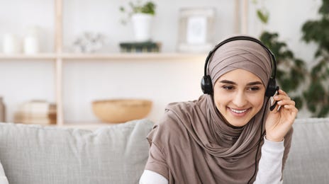 Femme avec des écouteurs dans son salon, prenant des notes tout en apprenant une nouvelle langue avec Berlitz Flex sur son ordinateur portable.