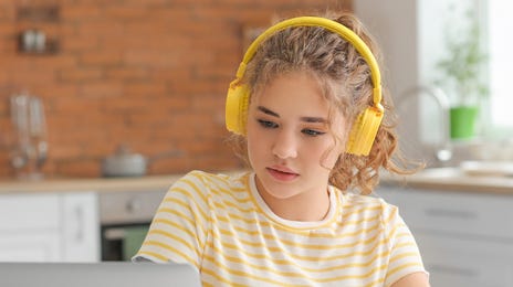 Fille avec un casque jaune prenant des notes pendant un cours d'anglais pour collégiens qu'elle suit à partir d'un ordinateur portable.