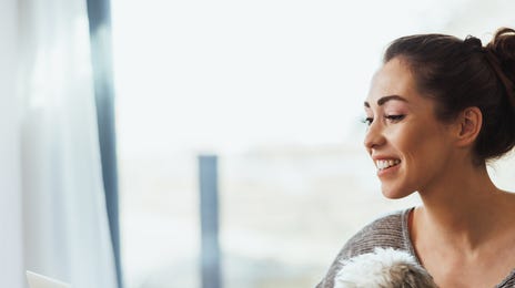Femme assise à son bureau avec son chien sur les genoux et apprenant des langues en ligne avec Berlitz sur son ordinateur portable.