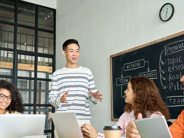Professeur debout à côté d'un tableau noir et s'adressant à ses élèves lors d'un de leurs cours de langue en groupe.