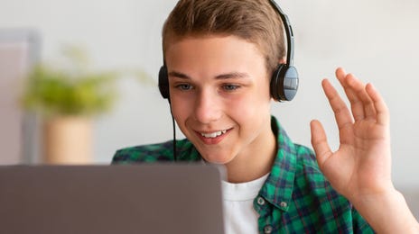 Un enfant fait signe à son professeur au début de son cours de langue en ligne pour adolescents.
