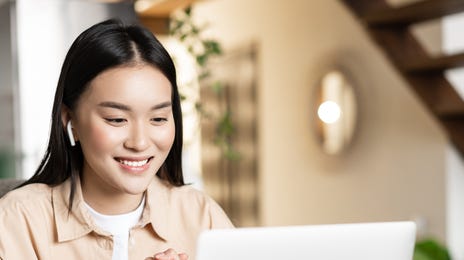 Adolescente souriant à son professeur à travers l'ordinateur portable pendant son cours d'allemand pour adolescent avec Berlitz France.