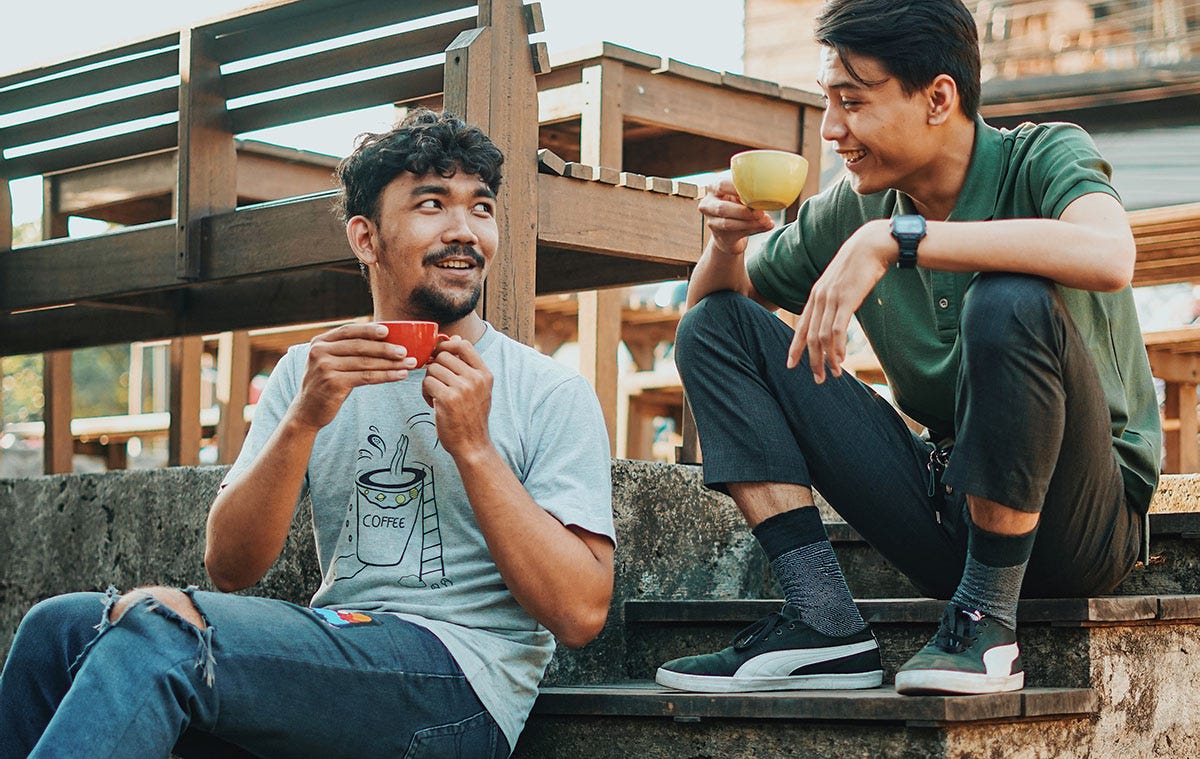 Two friendly man drinking coffee together outside of a coffee shop