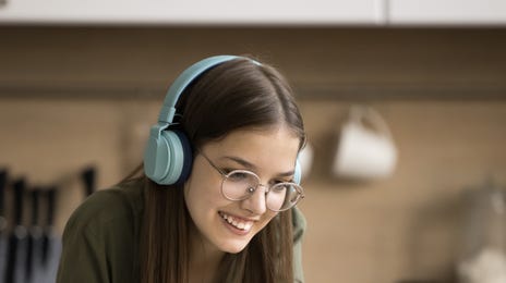 Une fille avec un casque sourit et prend des notes pendant une leçon de langue en ligne pour les enfants et les adolescents avec Berlitz France.