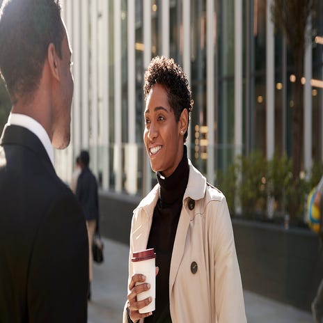 Woman holding a coffee cup and talking to her friend outside of a building after her TOEFL preparation course with Berlitz