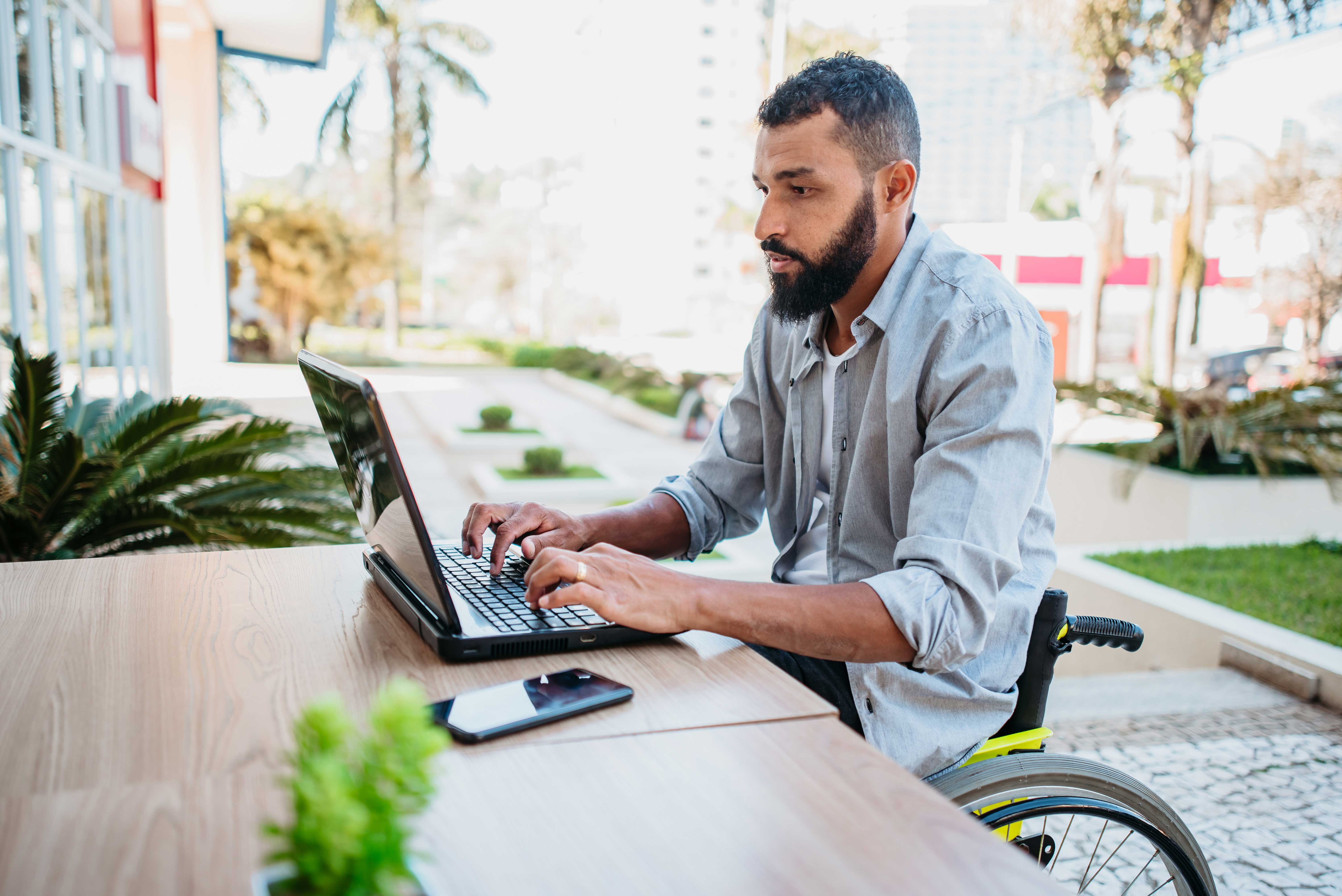 Man sitting at a table outside in a wheelchair and attending an online language course with Berlitz from his laptop