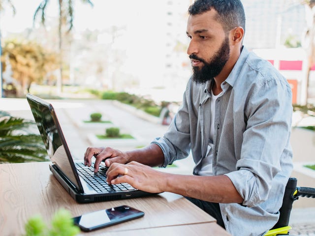 Man sitting at a table outside in a wheelchair and attending an online language course with Berlitz from his laptop
