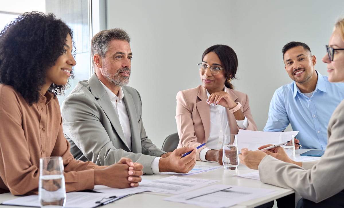 Employés assis à une table et écoutant leur formateur lors d'une formation linguistique en entreprise