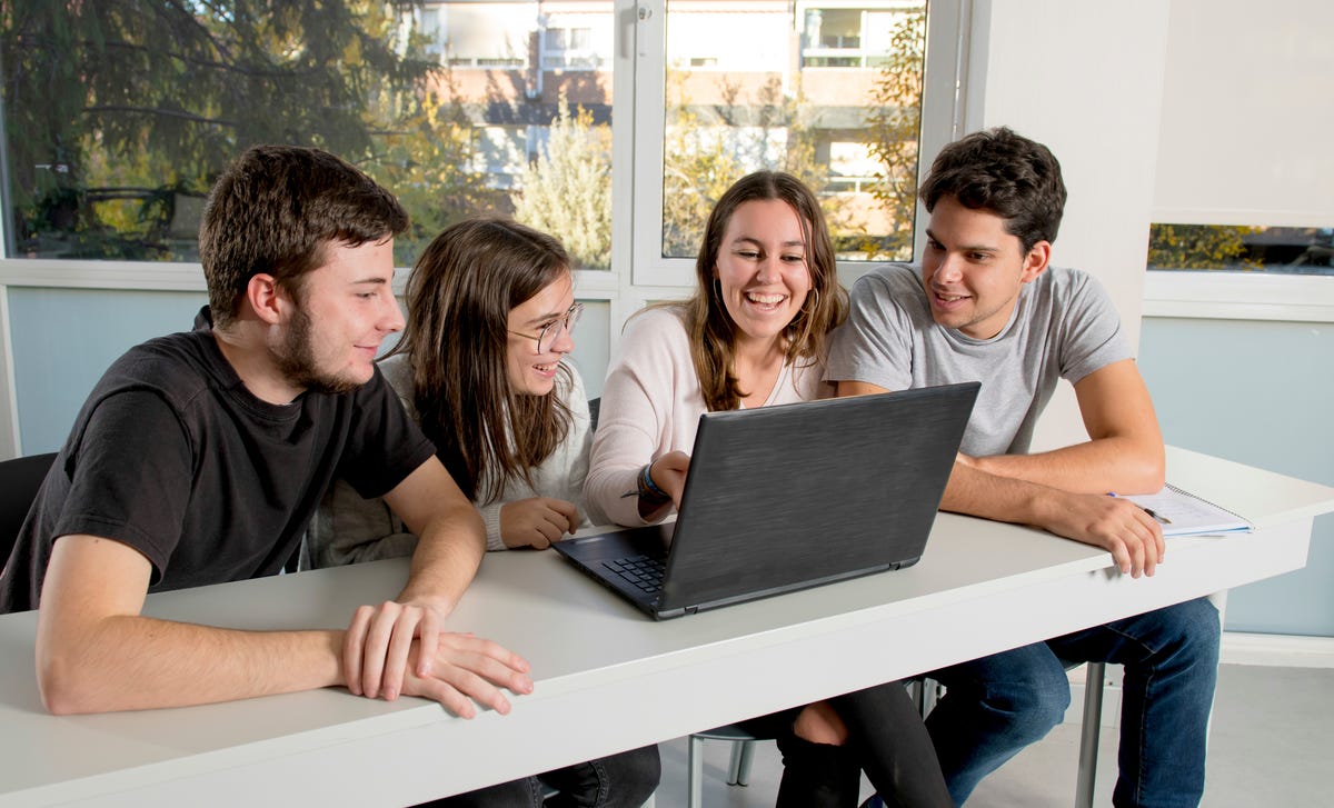 Enfants assis à une table devant un ordinateur portable et discutant du matériel de cours en allemand lors d'un cours d'allemand pour adolescent.