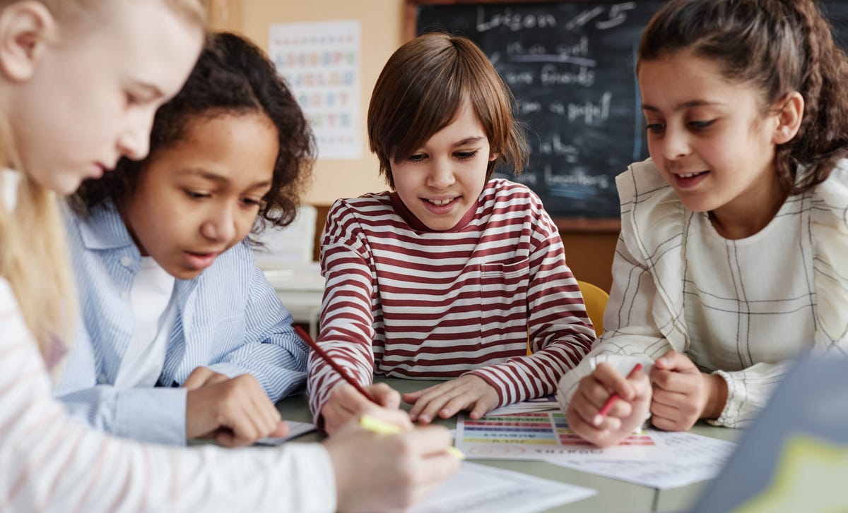 Groupe d'enfants assis autour d'une table et faisant des exercices de langue ensemble pendant un cours d'anglais pour enfants.