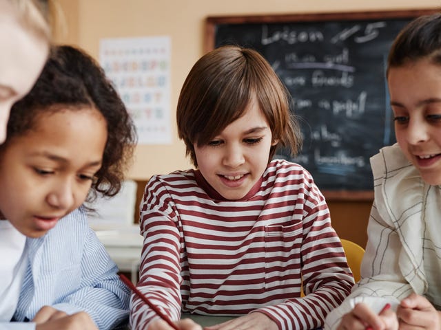 Groupe d'enfants assis autour d'une table et faisant des exercices de langue ensemble pendant un cours d'anglais pour enfants.