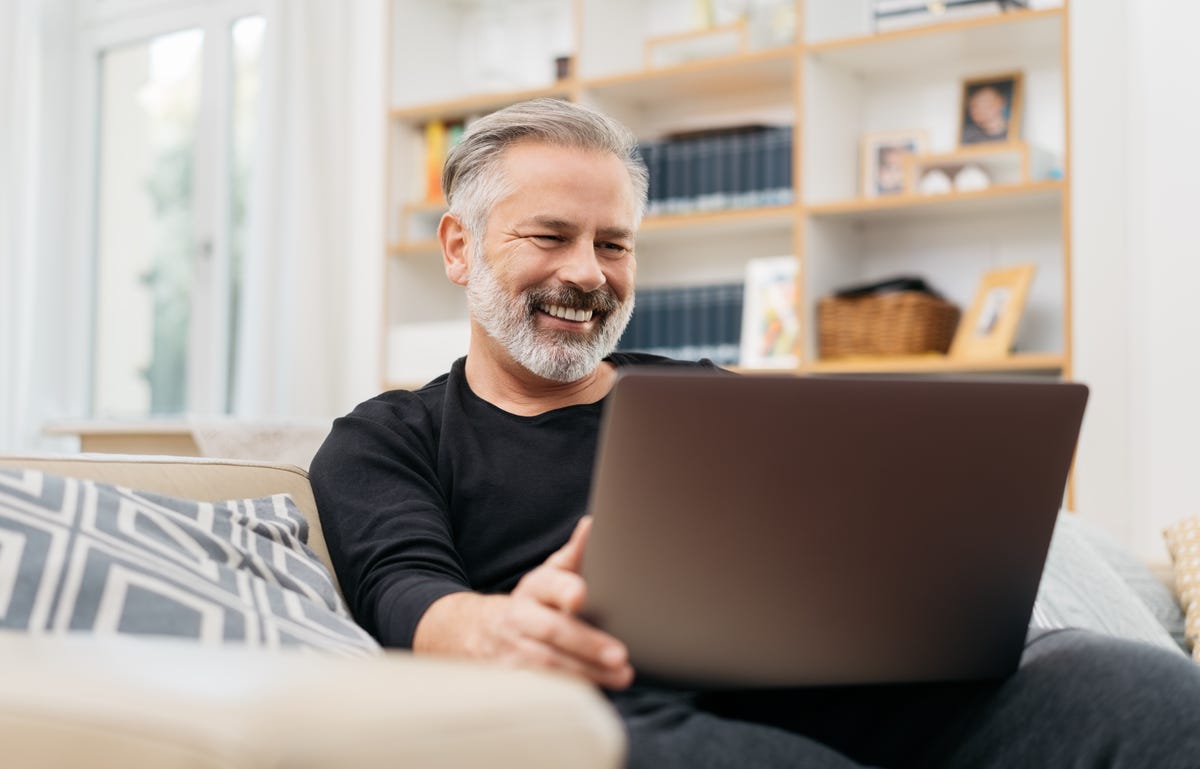 Man sitting on a couch holding a laptop in his lap and learning a language online with Berlitz Flex