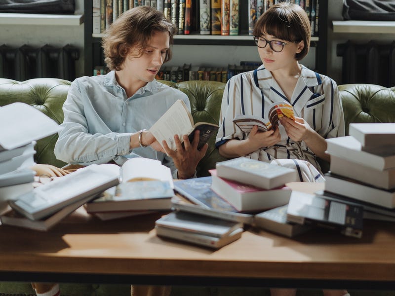 Deux étudiants assis sur un canapé, entourés de livres, apprennent ensemble l'alphabet espagnol et prononciation