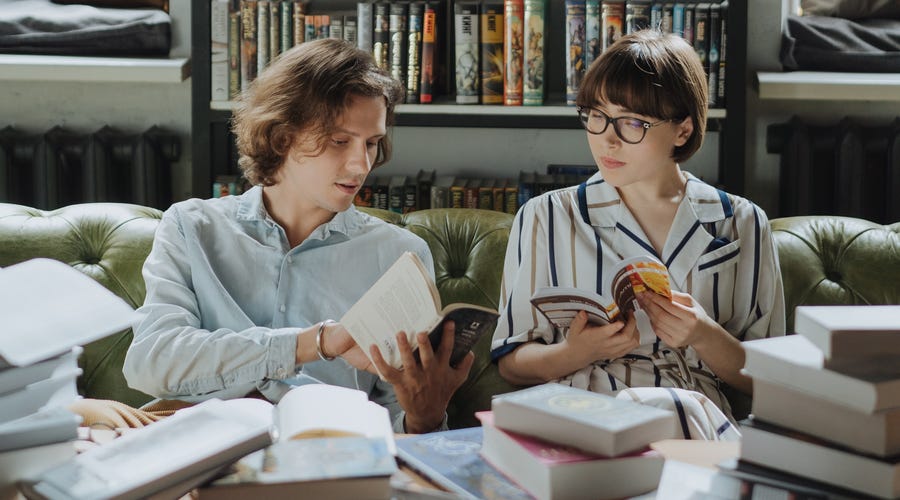 Two students sitting on a couch surrounded by books and learning the Spanish alphabet together