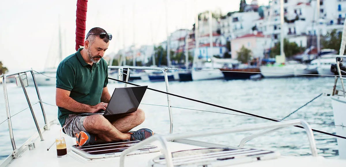 Man sitting on a ship writing a letter on his laptop during vacation