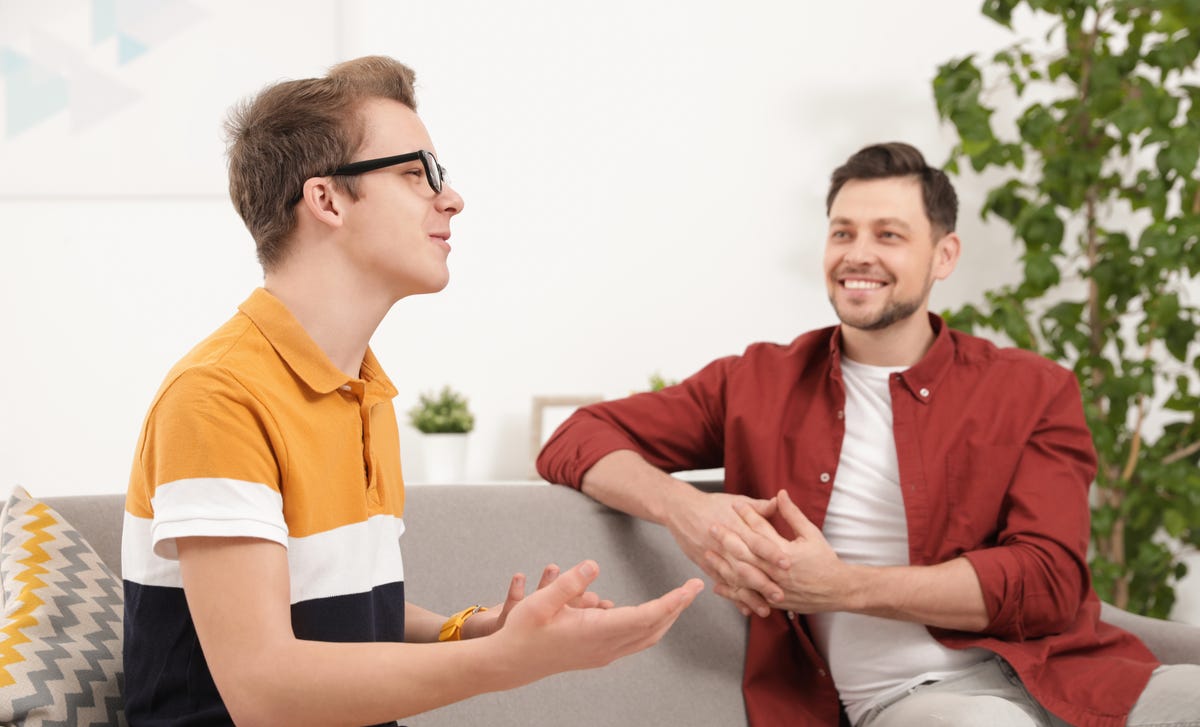 Adolescent assis à côté de son professeur sur un canapé et lui parlant dans la langue cible lors d'un cours de langue privé pour enfants et adolescents.