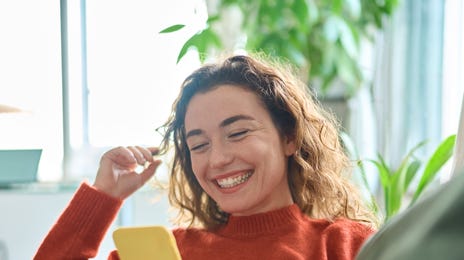 Femme assise sur un canapé et suivant un cours de langue à partir de son téléphone