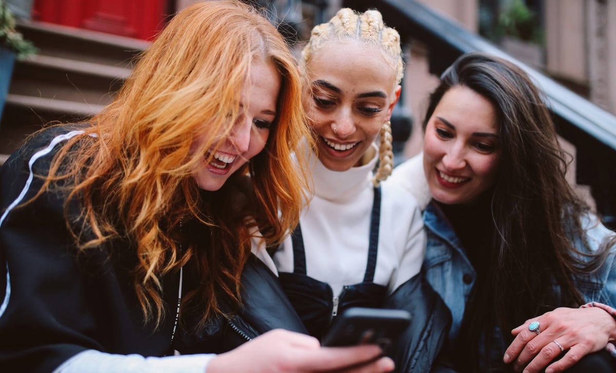 Girls looking at a phone and reading about how Berlitz works while smiling and talking to each other