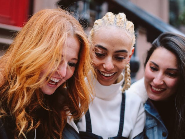 Des filles regardent un téléphone et lisent des informations sur le fonctionnement de Berlitz tout en souriant et en se parlant.