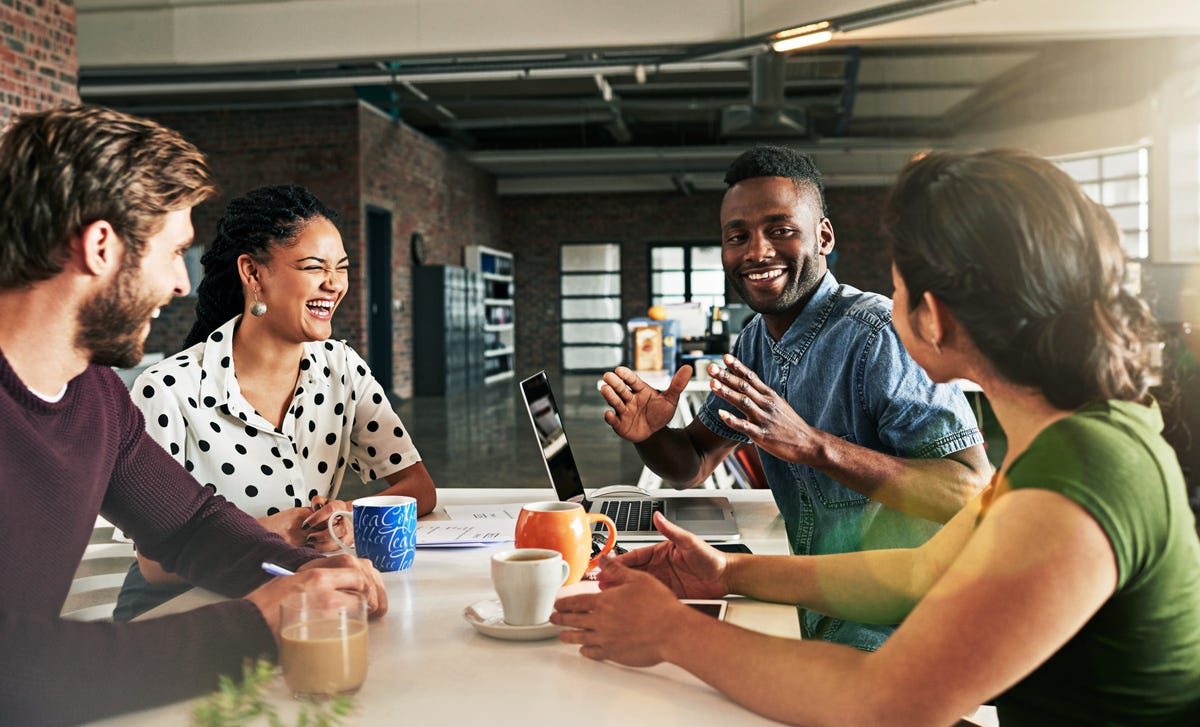 A group of students and their instructor sitting around a table with a laptop and coffee cups and talking to each other during an English class at Berlitz Lyon