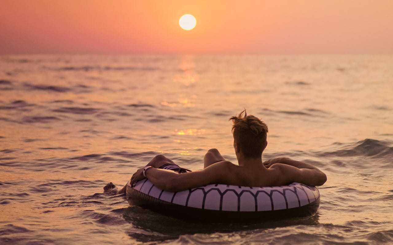 Man during the summer months swimming in the sea and looking at the sunset