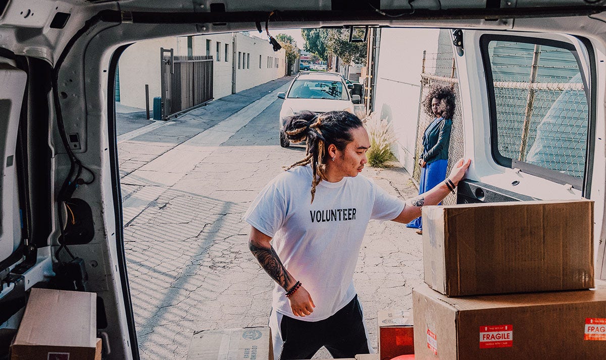 A happy man with a t-shirt that says 'Volunteer' opens the door of a car